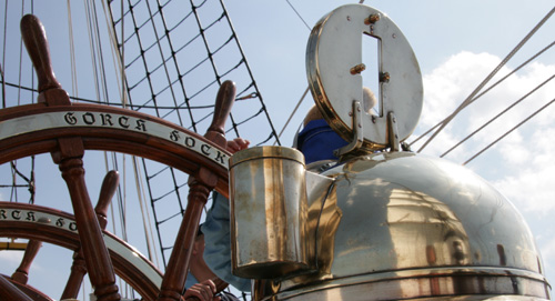 Die Segel der Gorch Fock spiegeln sich im Messinggehäuse nautischer Geräte