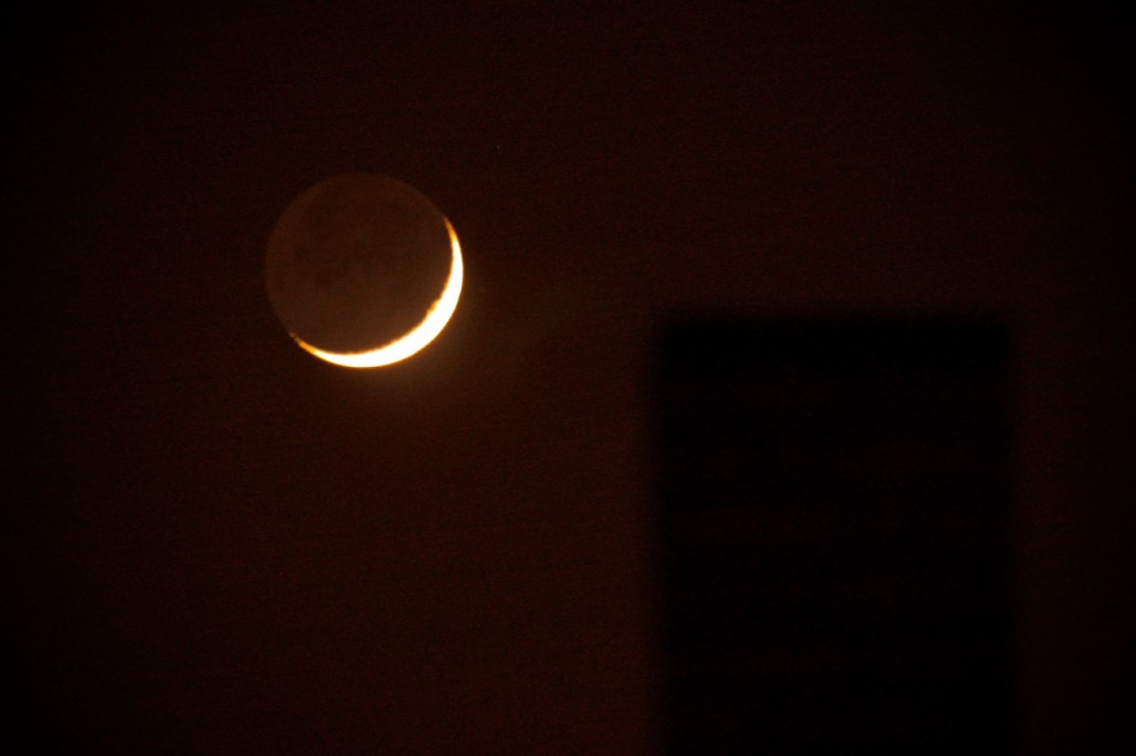 Dünne Mondsichel am rötlich schimmernden Nachthimmel.