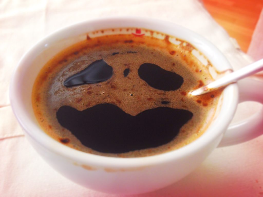 Kaffee in einer Tasse. Drei Löcher in der Crema sehen aus wie ein Gesicht mit zwei traurigen Augen