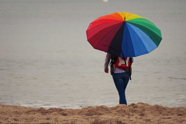 Frau mit buntem Regenschirm beim Strandspziergang.