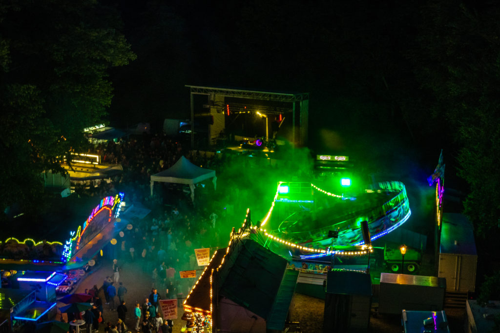 Blick aus einem Riesenratt auf einen bunt leuchtenden Rummel abends