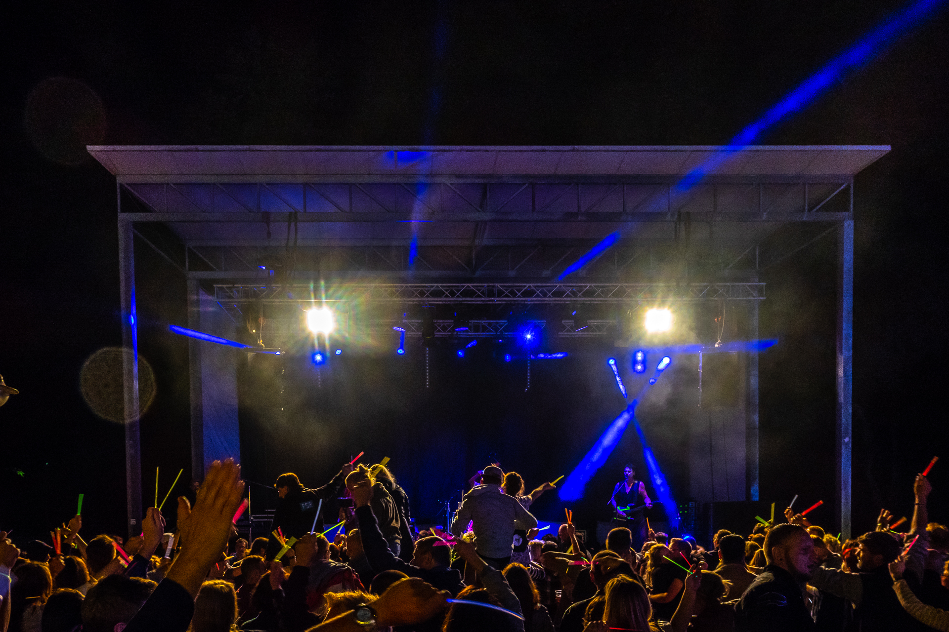 Publikum vor einer nächtlichen Musikbühne mit blauen Scheinwerferstrahlen