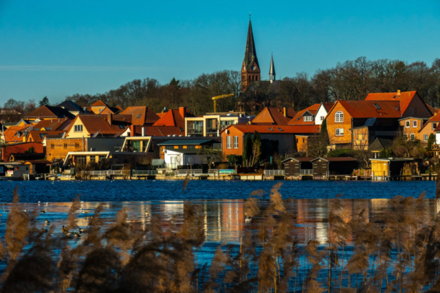 Malchower Kirche, davor der dünn mit Eis bedeckte See, Fassaden leuchten in der Sonne