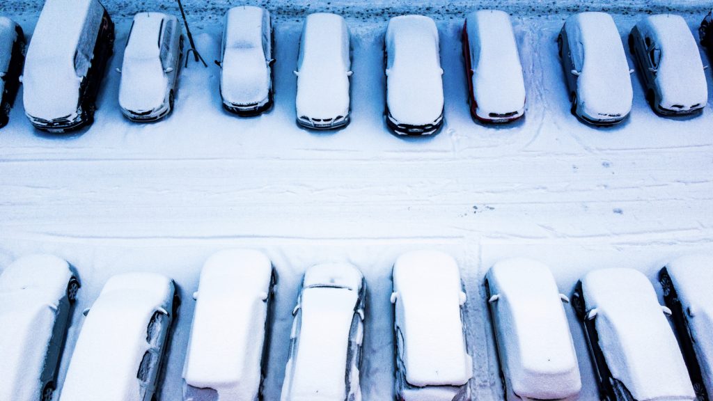 Schneebedeckte Autos parken auf beiden Straßenseiten, von oben gesehen.