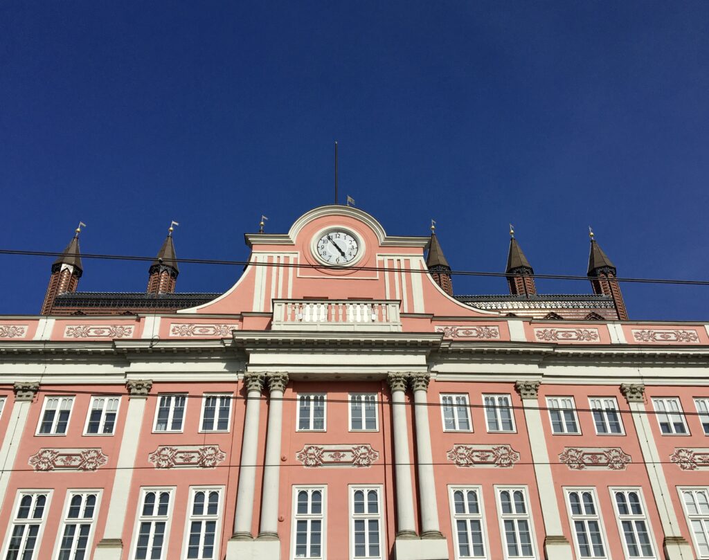 Die rosa Fassade mit weißen Elementen, im Sonnenlicht. Der tiefblaue Himmel spiegelt sich in den Fenstern.