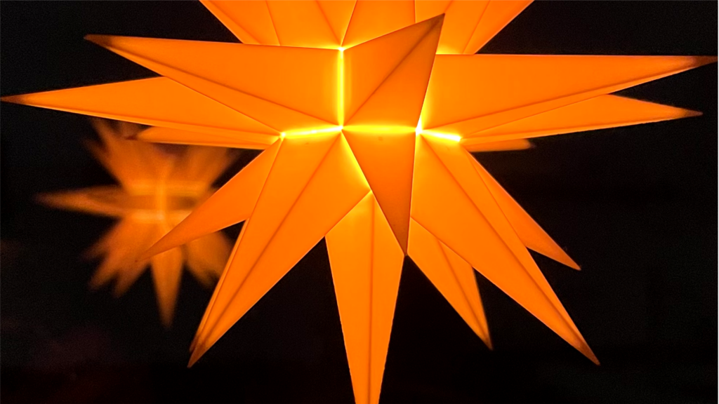 Ein gelb leuchtender Weihnachtsstern spiegelt sich in einer Glasscheibe.