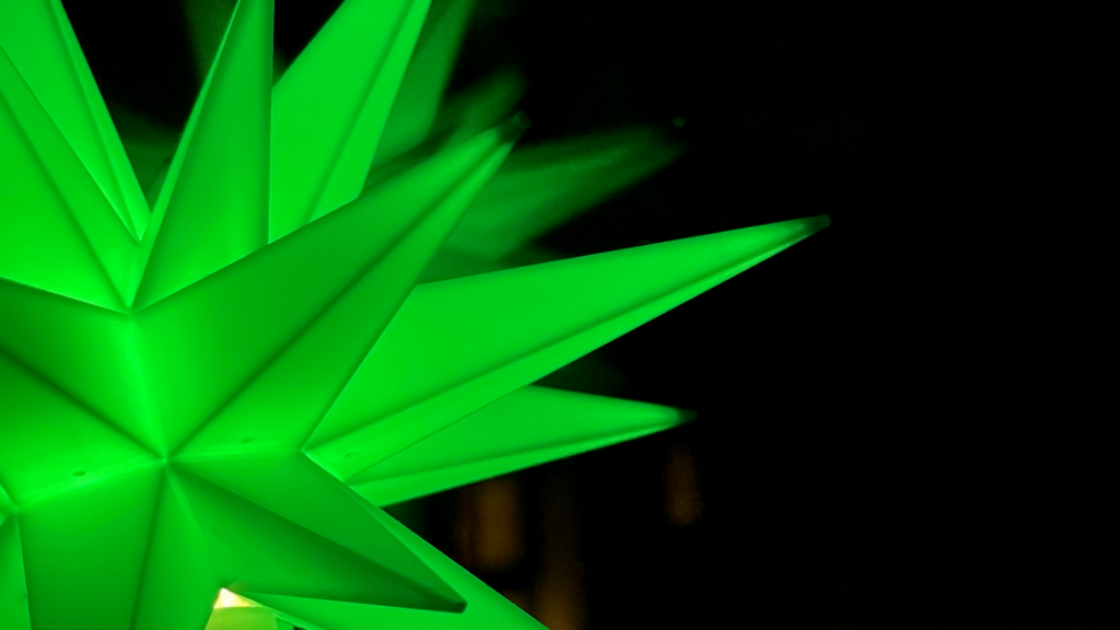 Nahaufnahme eines grün leuchtenden Weihnachtssterns zeigt einige Spitzen.